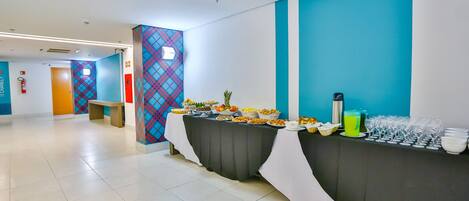 A buffet setup with various food items and drinks, a tiled floor, and a blue and white wall design.
