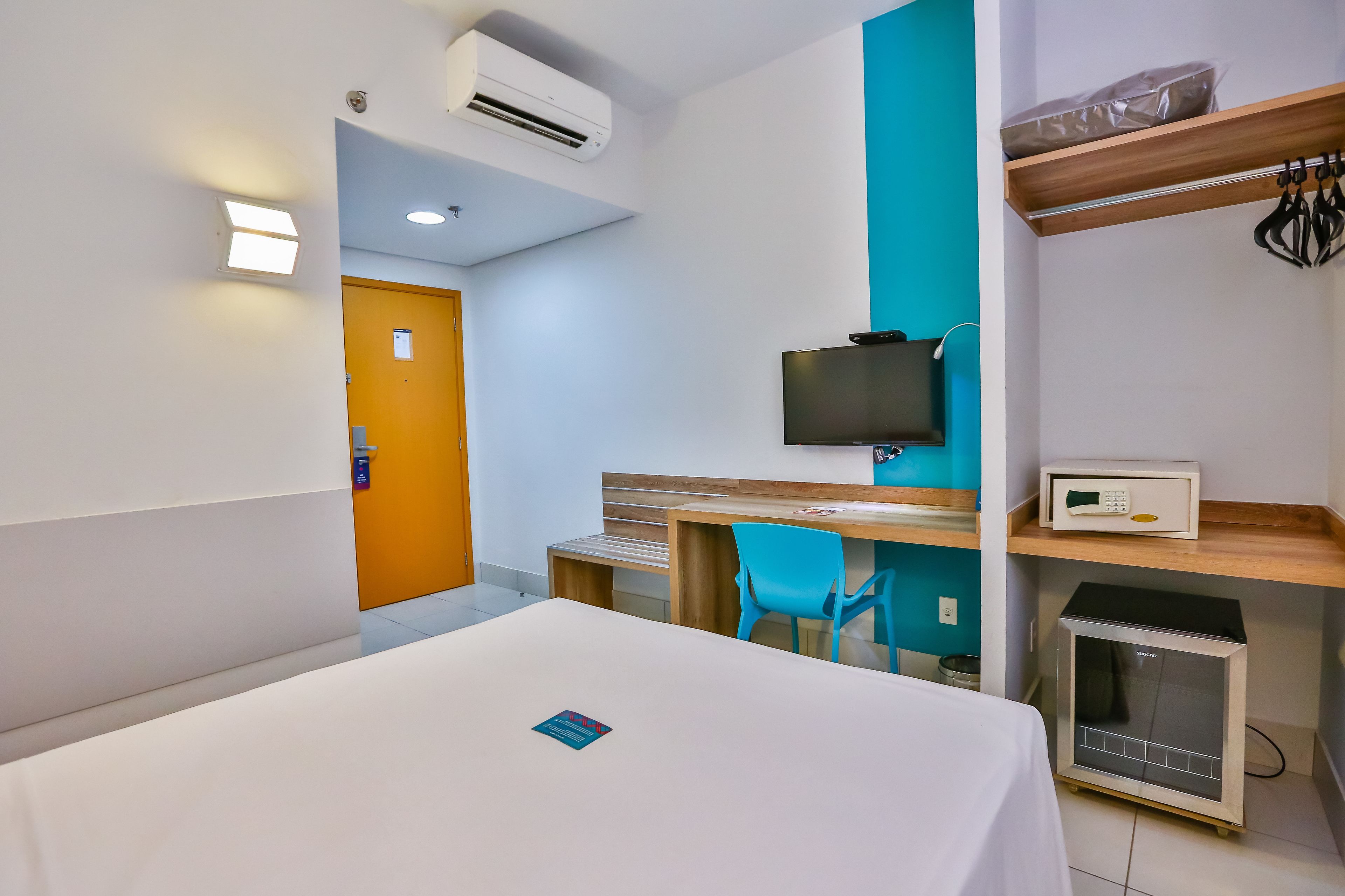 A hotel room with a bed, a desk with a chair, a television, a microwave, and a small refrigerator.