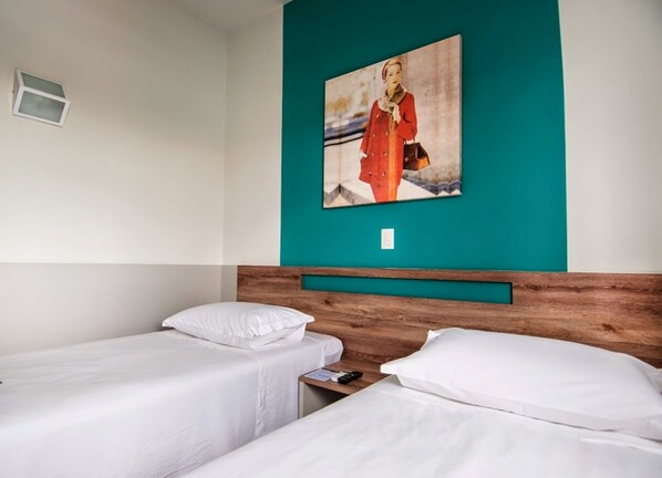 A hotel room with two single beds, a wooden headboard, a teal accent wall, and a framed picture of a person in a red coat.