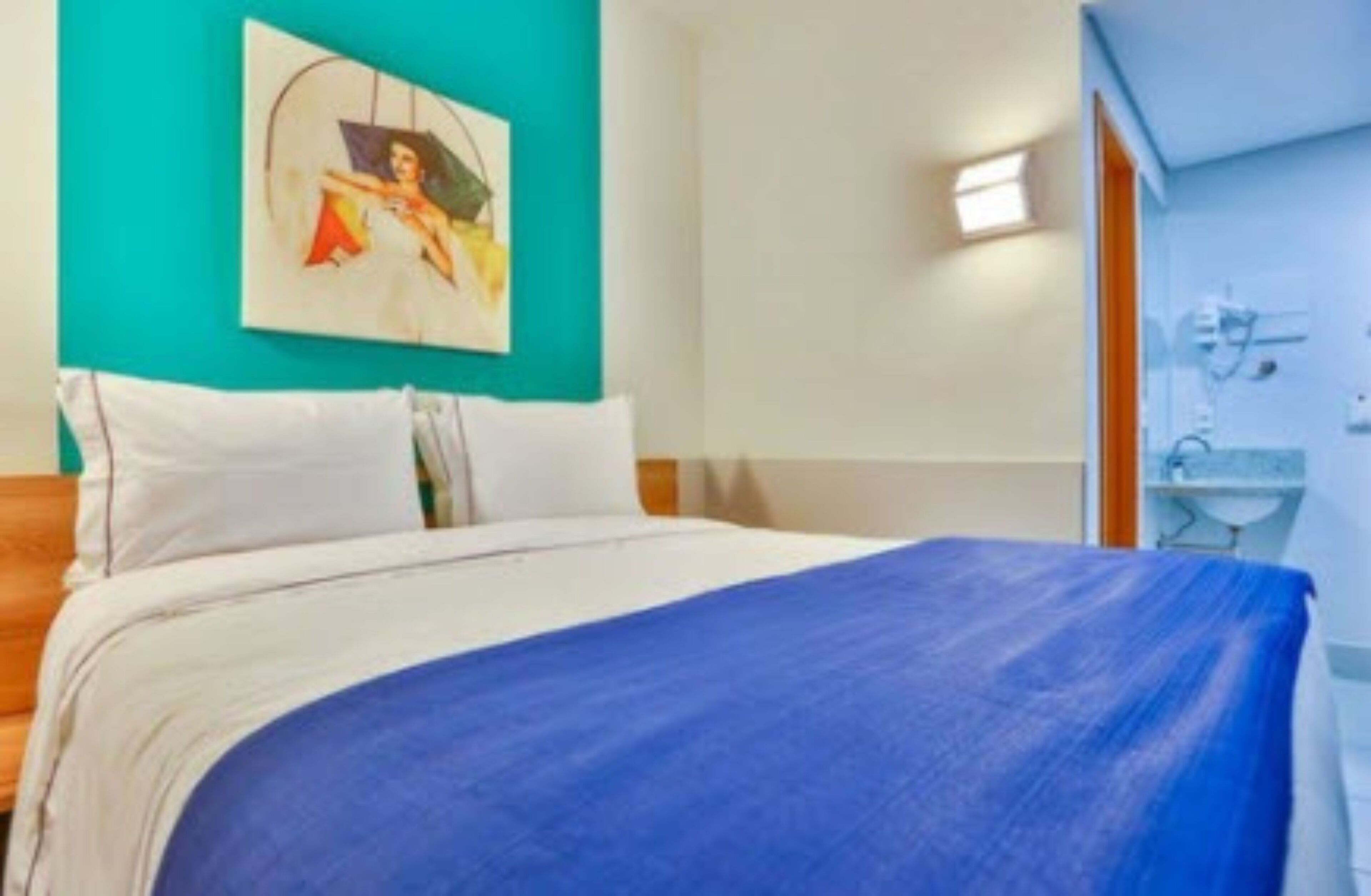 Een hotelkamer met een bed, een schilderij aan de muur en een badkamer met een wastafel en spiegel.