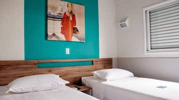 Una habitación de hotel con dos camas individuales, un cabecero de madera, una pared de acento color aguamarina, un cuadro, una ventana con persianas y una mesita de noche pequeña.
