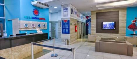 A modern hotel lobby with a reception desk, a digital screen, and a blue wall with a logo.