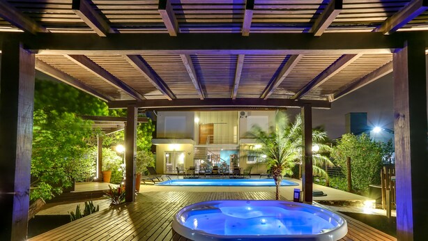Un área de hidromasaje al aire libre con un muelle de madera, una piscina y una zona de estar cubierta con mesas y sillas.