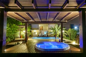An outdoor hot tub area with a wooden deck, a pool, and a covered seating area with tables and chairs. - Pousada Ilha Faceira (Florianópolis)