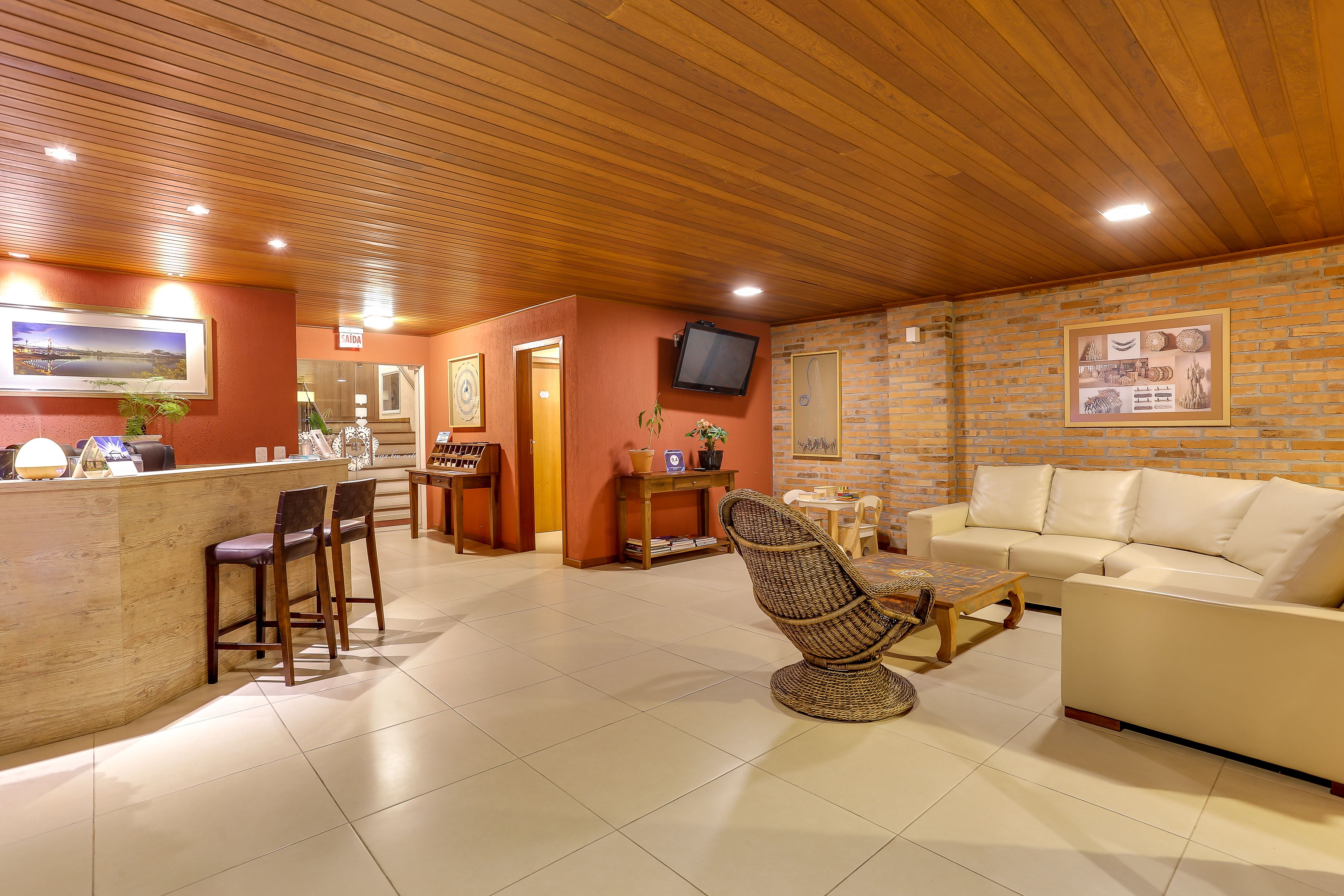A cozy interior with a wooden ceiling, a reception desk, a sofa, and a wicker chair.
