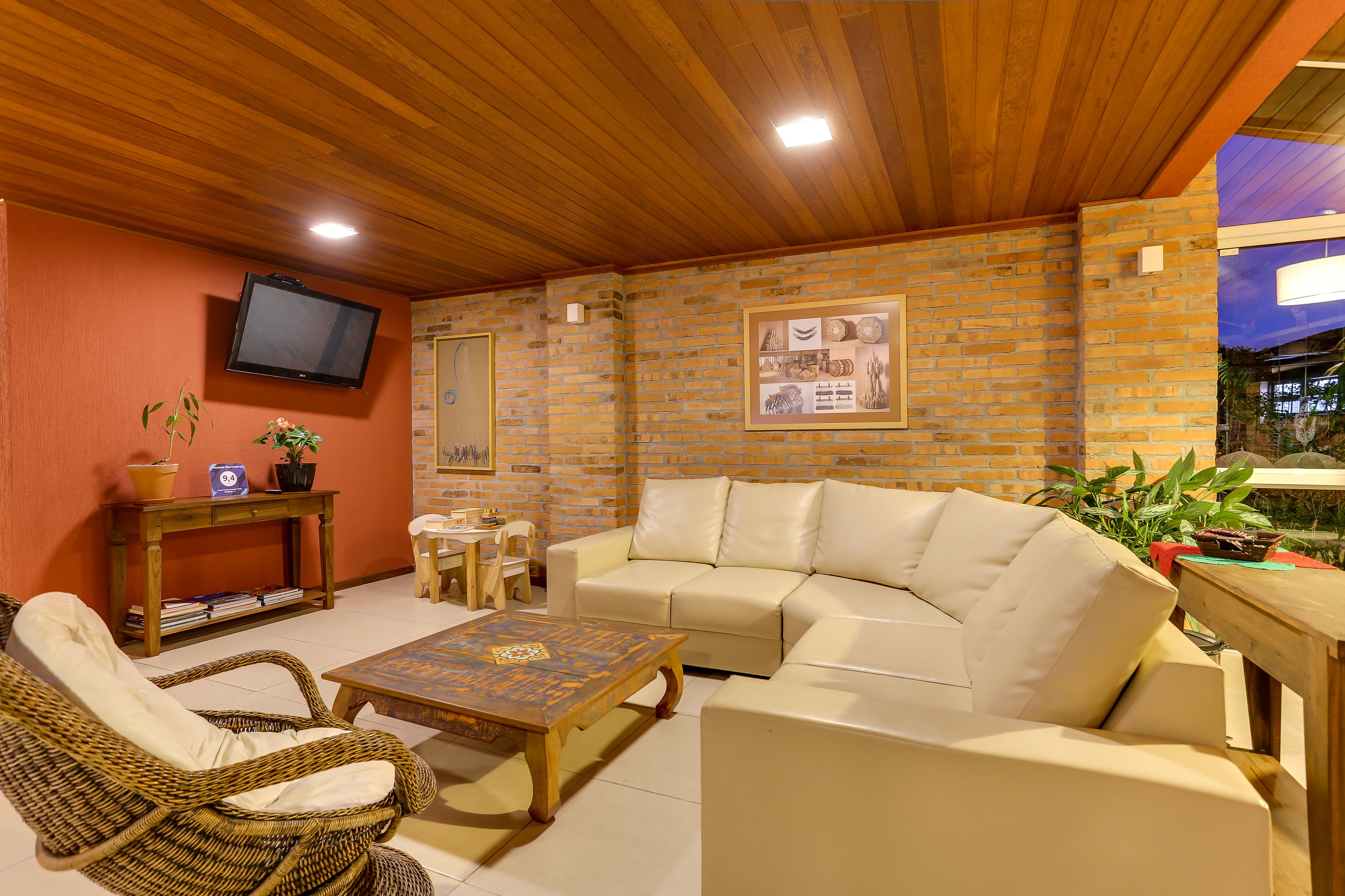 A cozy outdoor seating area with a wooden ceiling, a brick wall, a television mounted on the wall, and a table with chairs.
