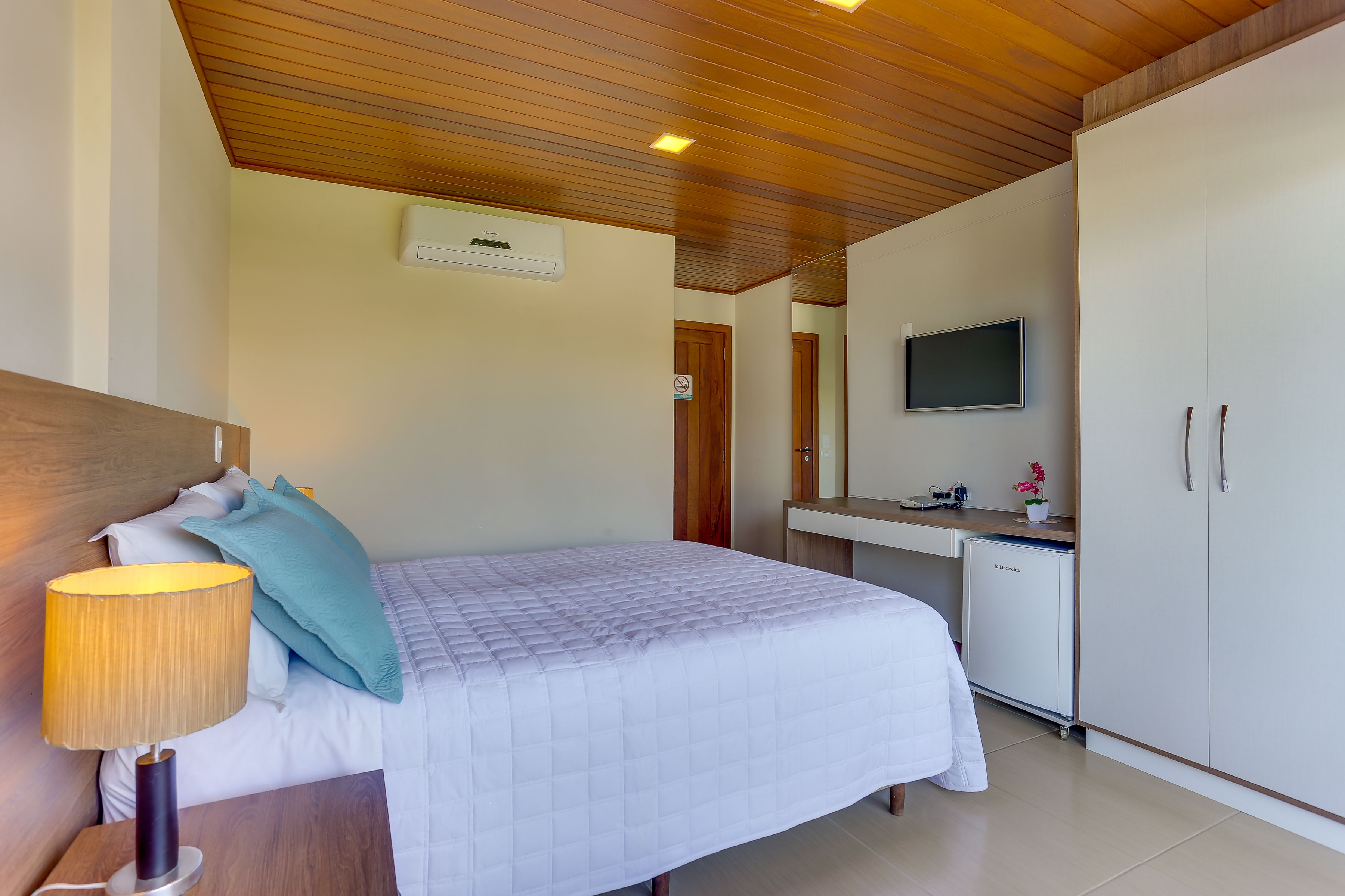 A bedroom with a bed, bedside lamp, and a desk with a TV and a small fridge.