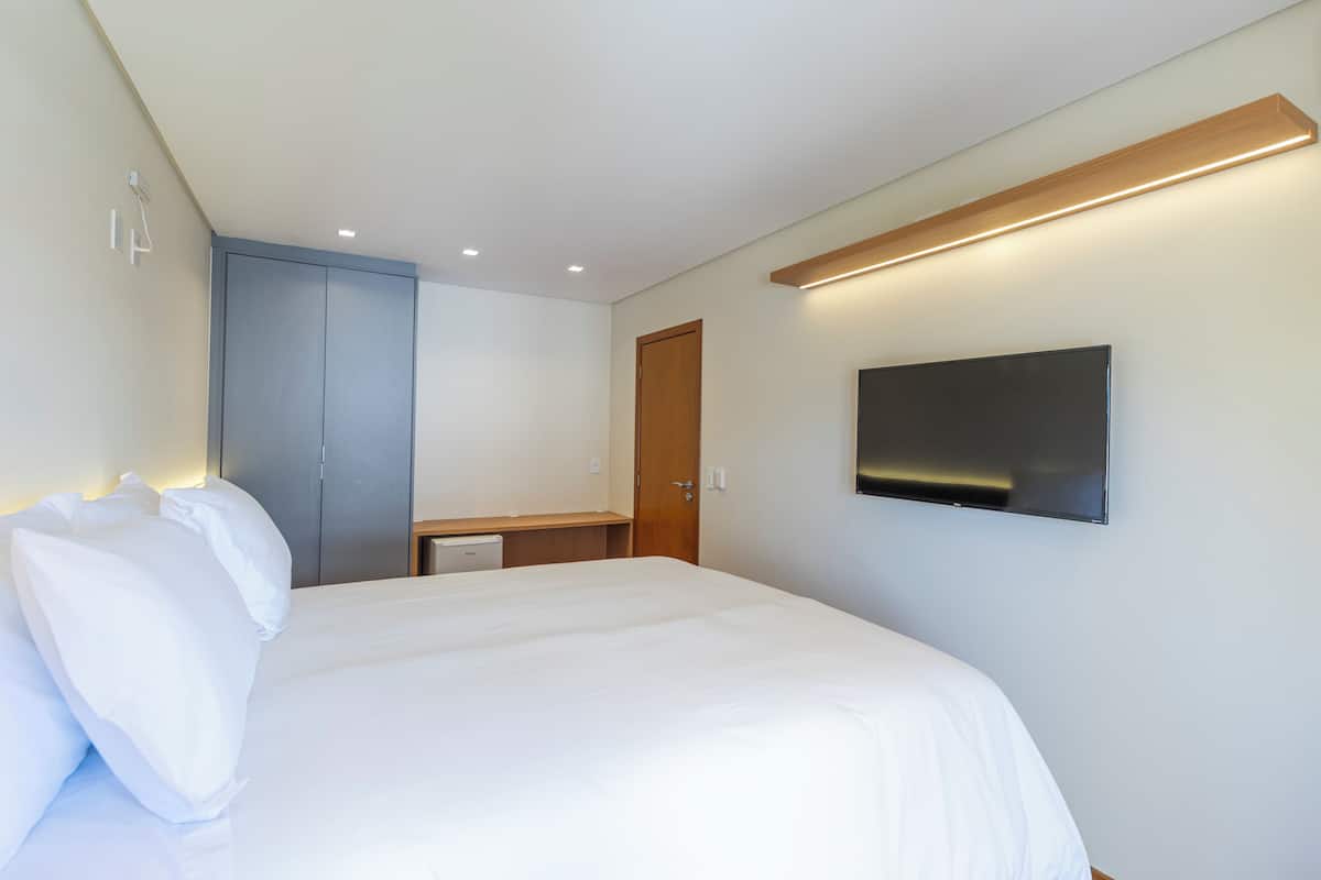 A hotel room with a large bed, a TV mounted on the wall, and a wardrobe.