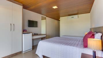 Quarto com cama, mesa de cabeceira, escrivaninha, guarda-roupa e televisão fixada na parede.
