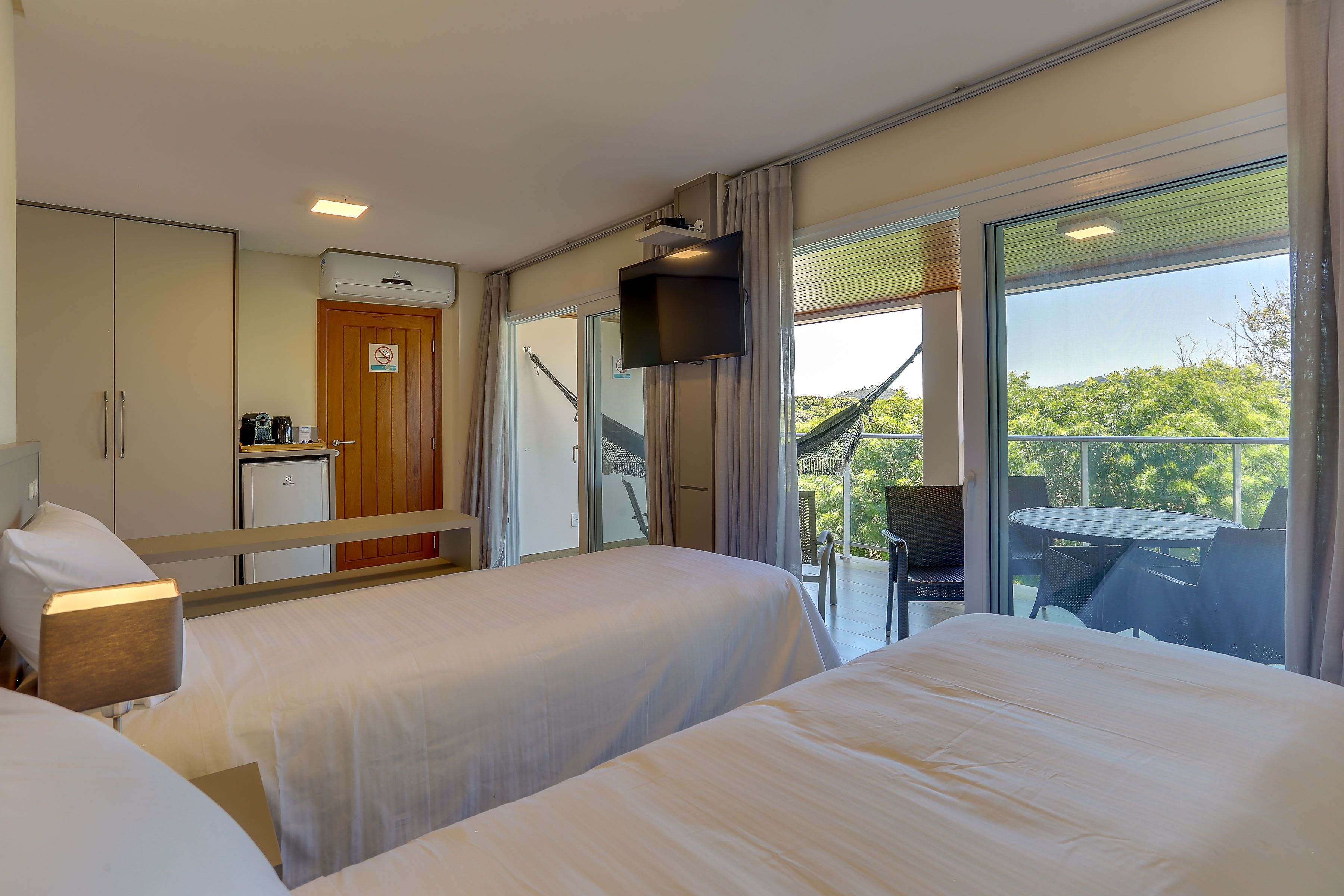 Habitación de hotel con dos camas, kitchenette, televisor y balcón con mesa y sillas.