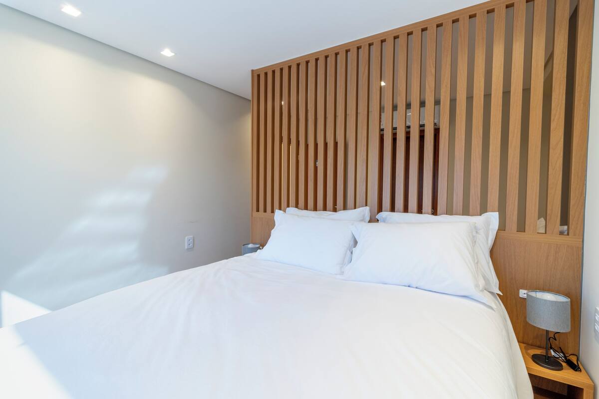 A modern hotel room with a large bed, wooden headboard, and a bedside table with a lamp.