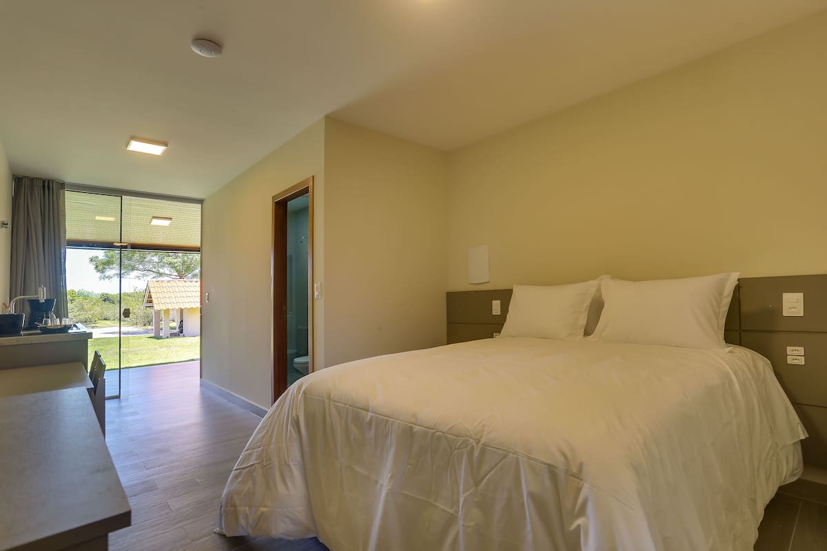 A bedroom with a large bed, a desk, and a view of a garden through a glass door.