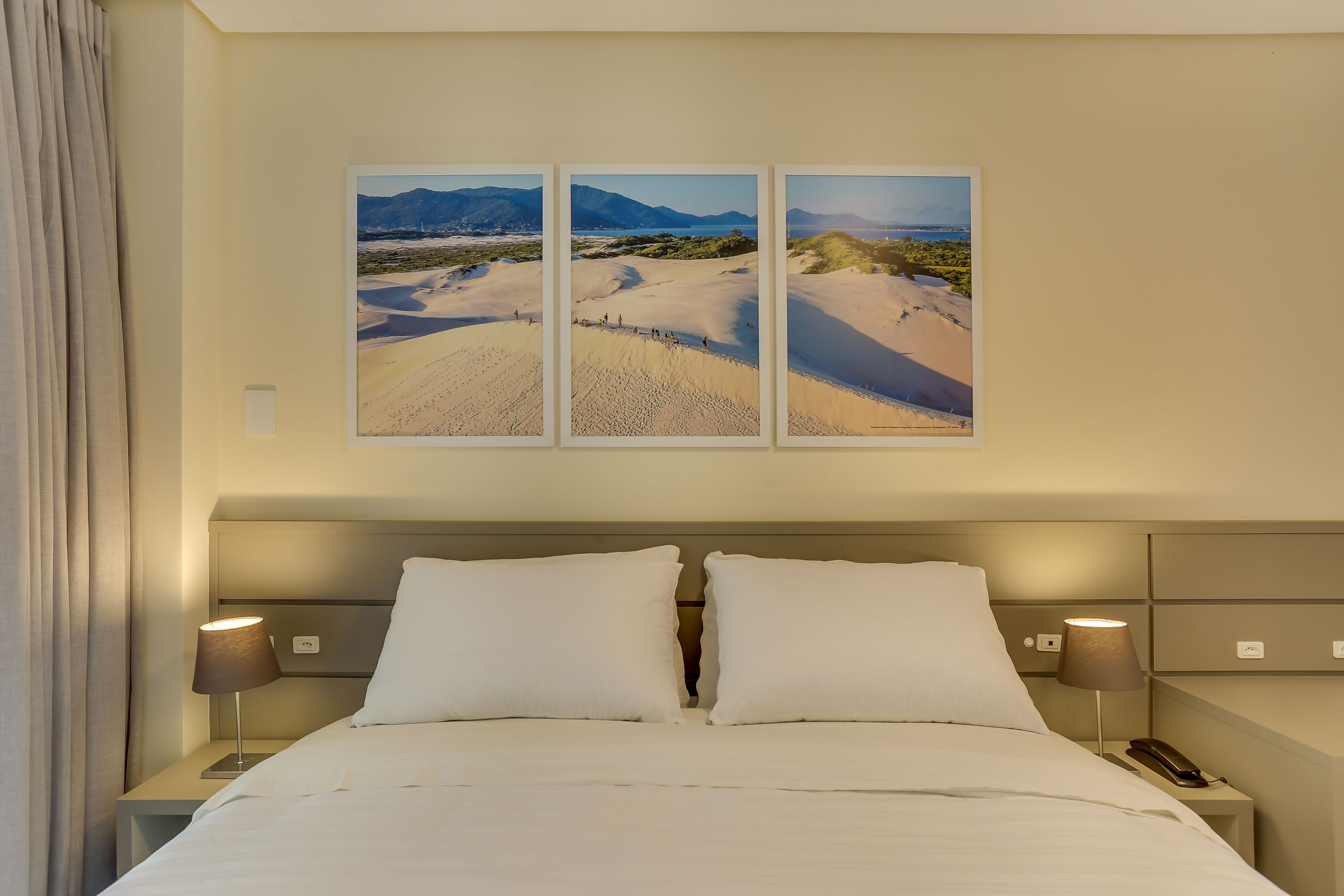 A hotel room with a large bed, two bedside lamps, a phone on the nightstand, and a wall-mounted picture of a desert landscape.