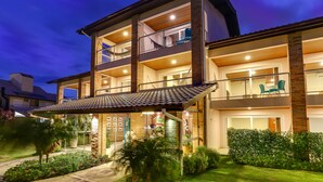 Un edificio residencial de varios pisos con balcón, patio cubierto y jardín cuidado.