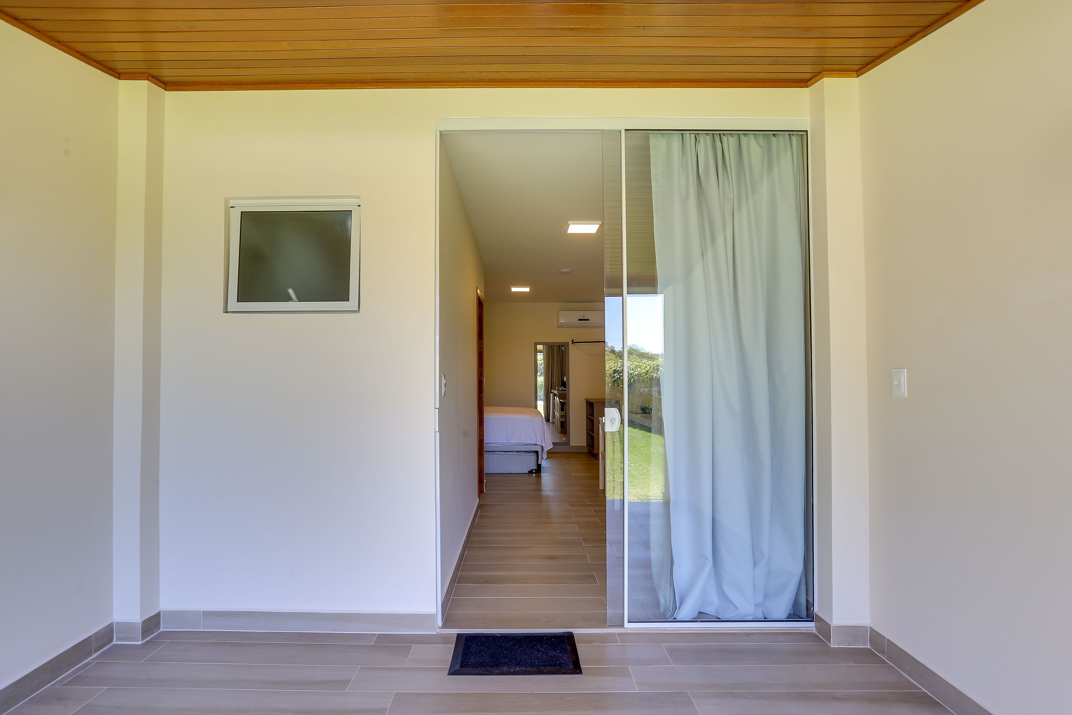 A hallway leading to a bedroom with a sliding glass door, a small window, and a black doormat.