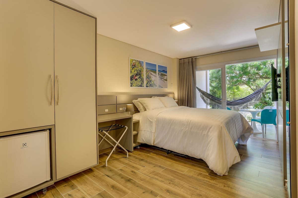 A bedroom with a bed, a wardrobe, a desk, and a view of the outdoors.