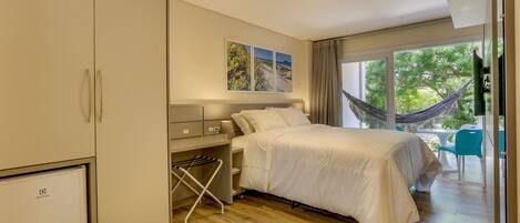 A bedroom with a bed, a wardrobe, a desk, and a view of the outdoors.