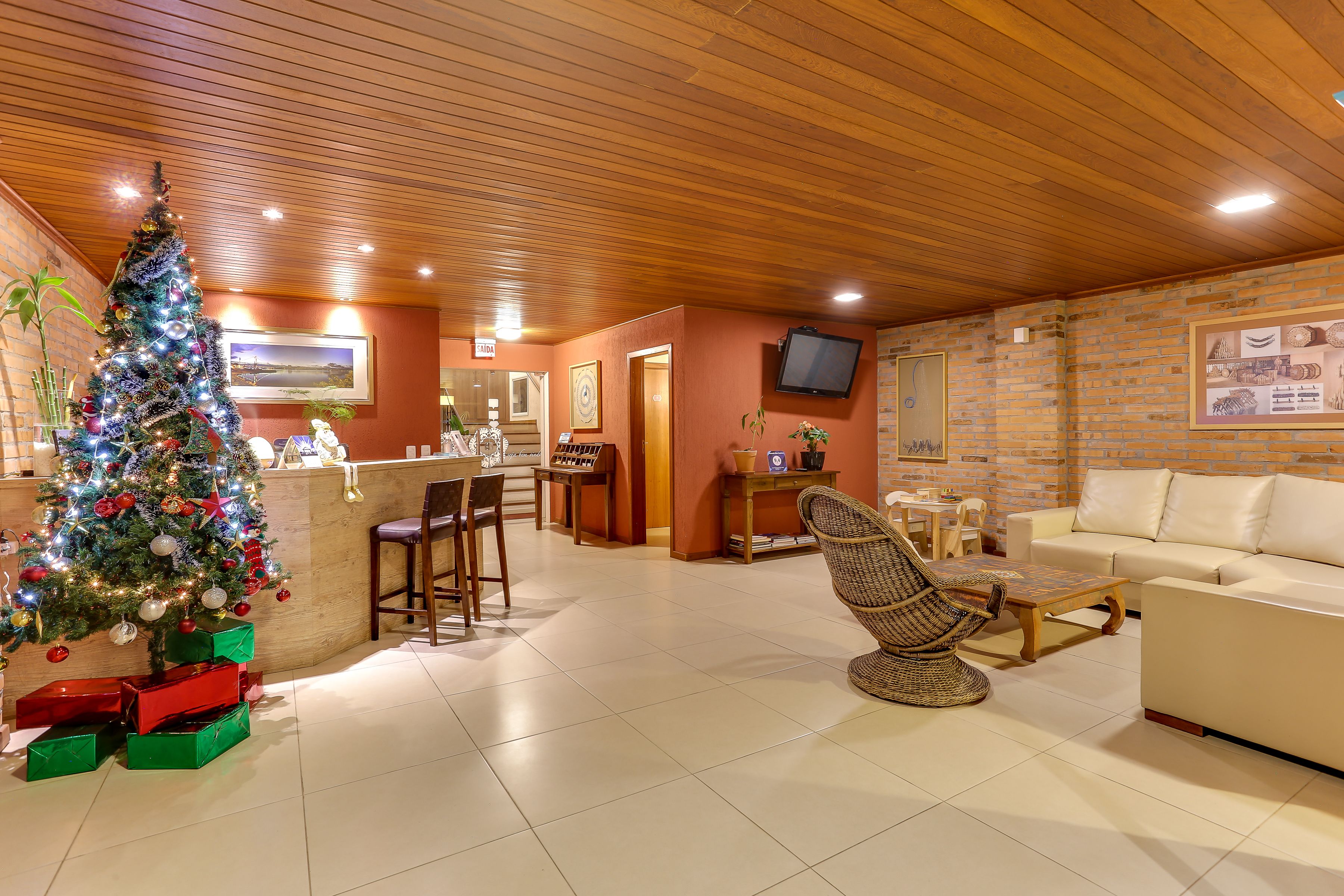 Una sala de estar acogedora con techo de madera, un árbol de Navidad, un sofá y un sillón de mimbre.