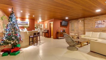 Una sala de estar acogedora con techo de madera, un árbol de Navidad, un sofá y un sillón de mimbre.