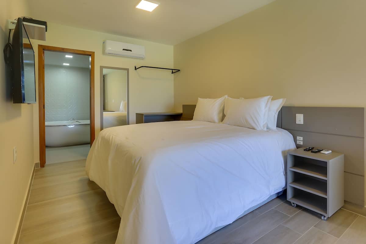 A hotel room with a large bed, bedside tables, a TV, a mirror, and a small shelf.