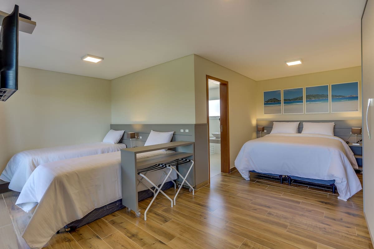 A hotel room with two beds, a desk, a chair, a TV, and artwork on the wall.