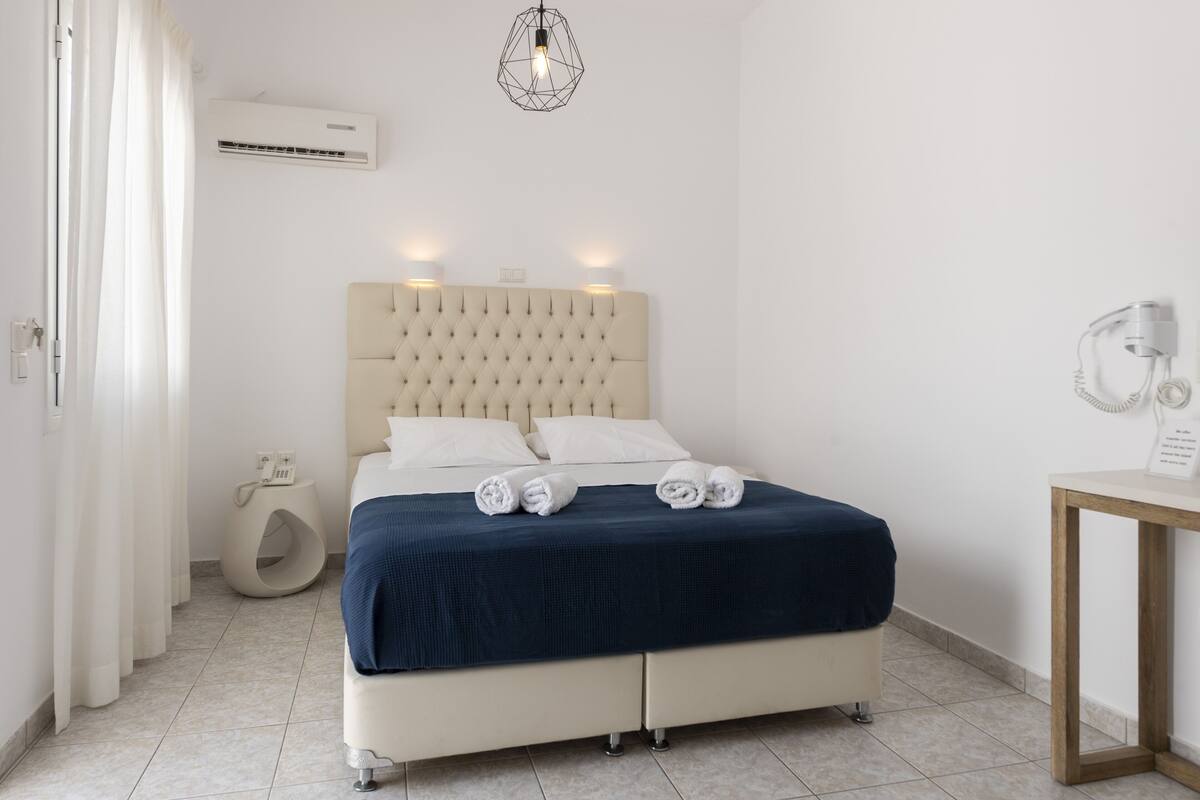 A neatly arranged bedroom with a bed, bedside table, and an air conditioning unit.