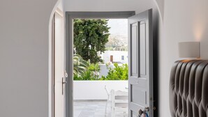 Un dormitorio con cama, cabecera y vista a un patio exterior con una silla blanca y vegetación.