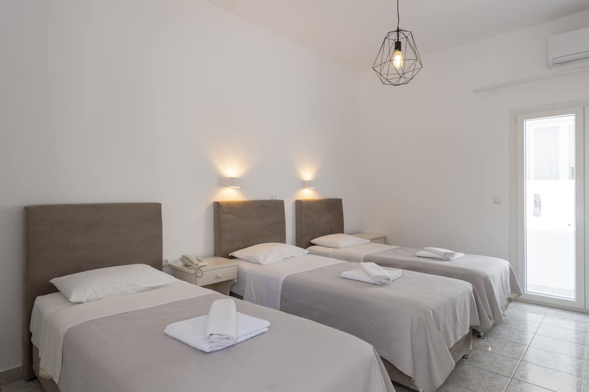A hotel room with three beds, each with a headboard and bedside tables. There is a hanging light fixture above the beds.