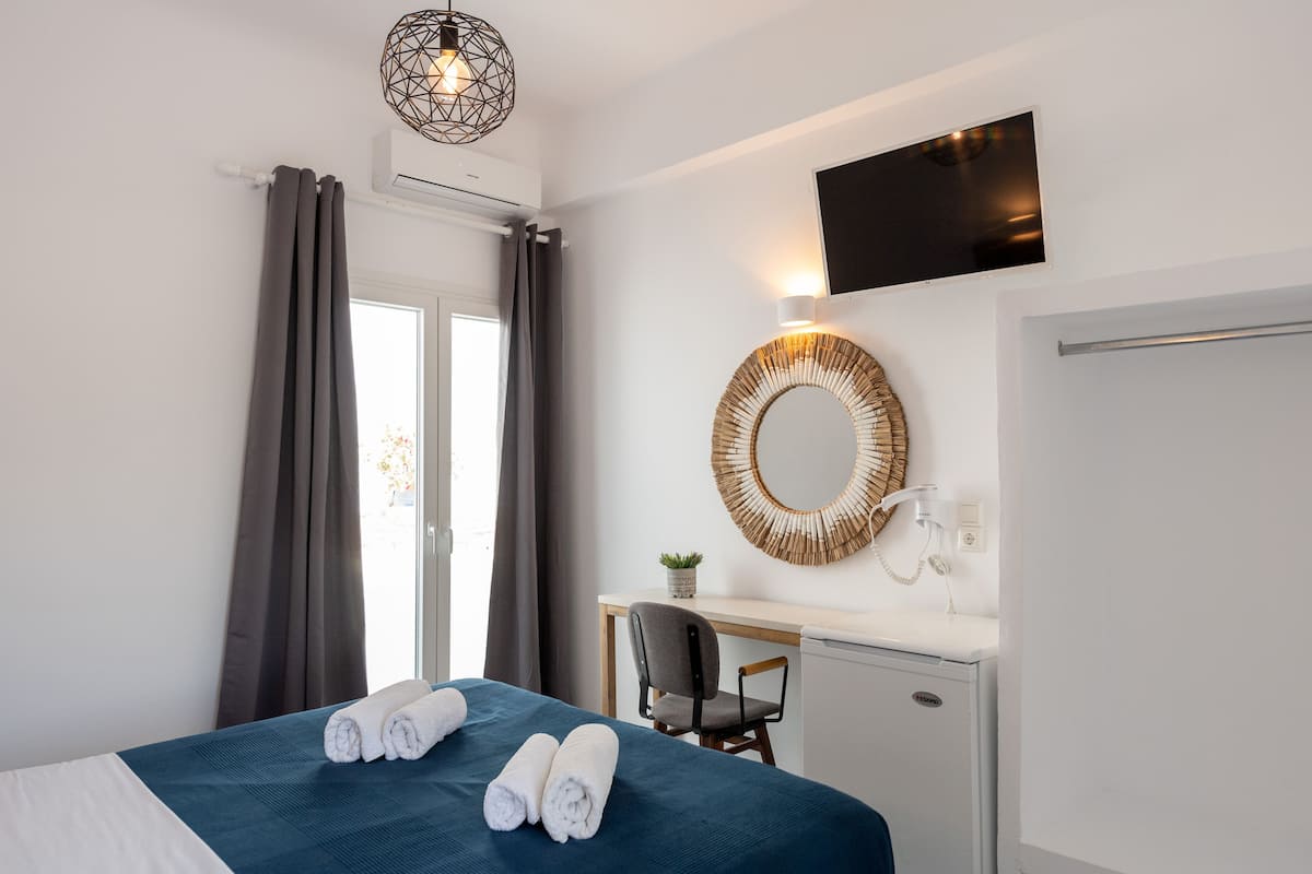 A hotel room with a bed, a desk, a chair, a TV, a mirror, and a window with curtains.