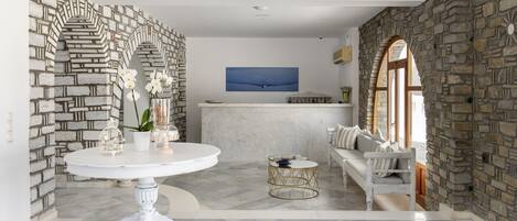 A spacious room with a white round table, a white sofa, and a stone wall.
