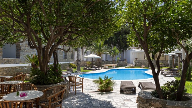 Un área de piscina con sillas de descanso y mesas, rodeada de muros de piedra y vegetación.