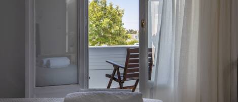 A bedroom with a bed, a white towel, and a view of a tree through an open door.