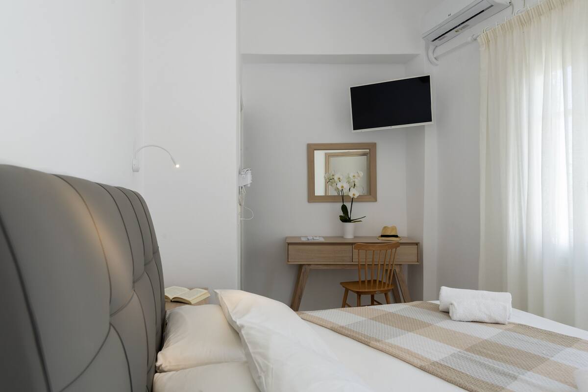 A hotel room with a bed, a desk, a chair, a TV, and a window with curtains.