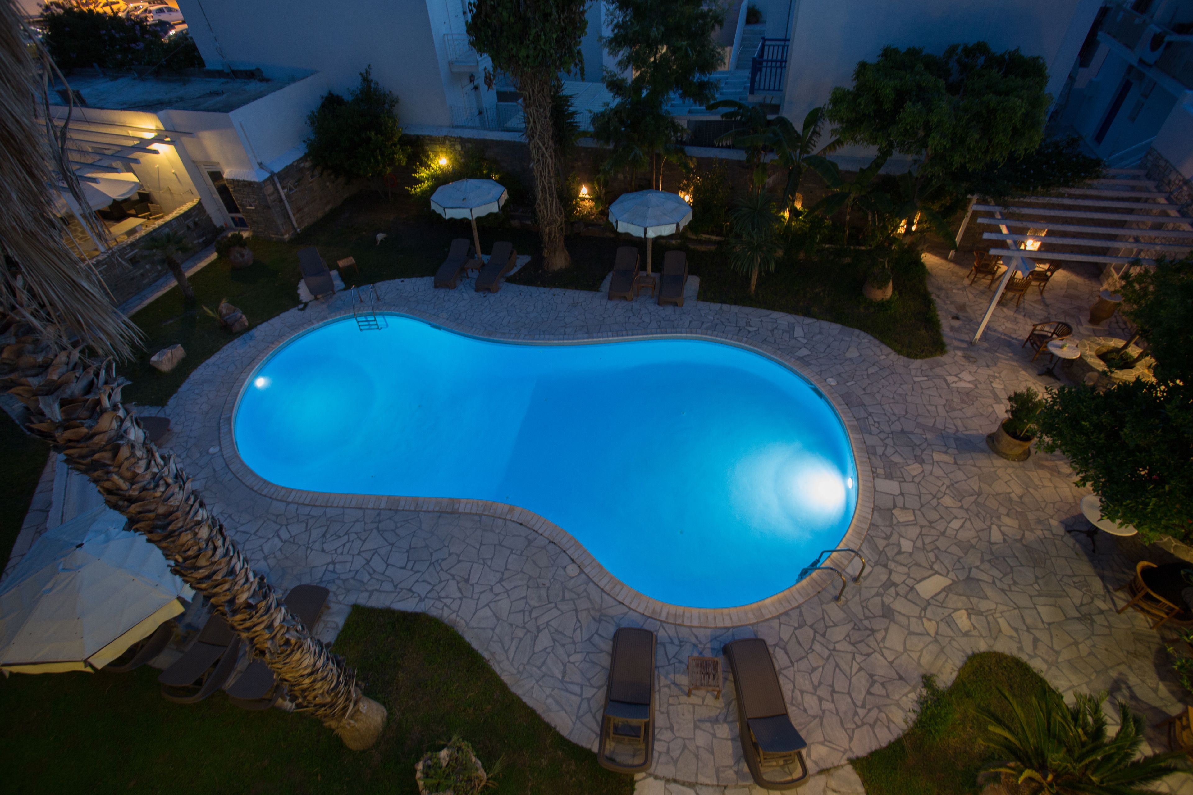 Ein Swimmingpool, umgeben von Liegestühlen und Sonnenschirmen, mit Steinböden und einer Steinwand.