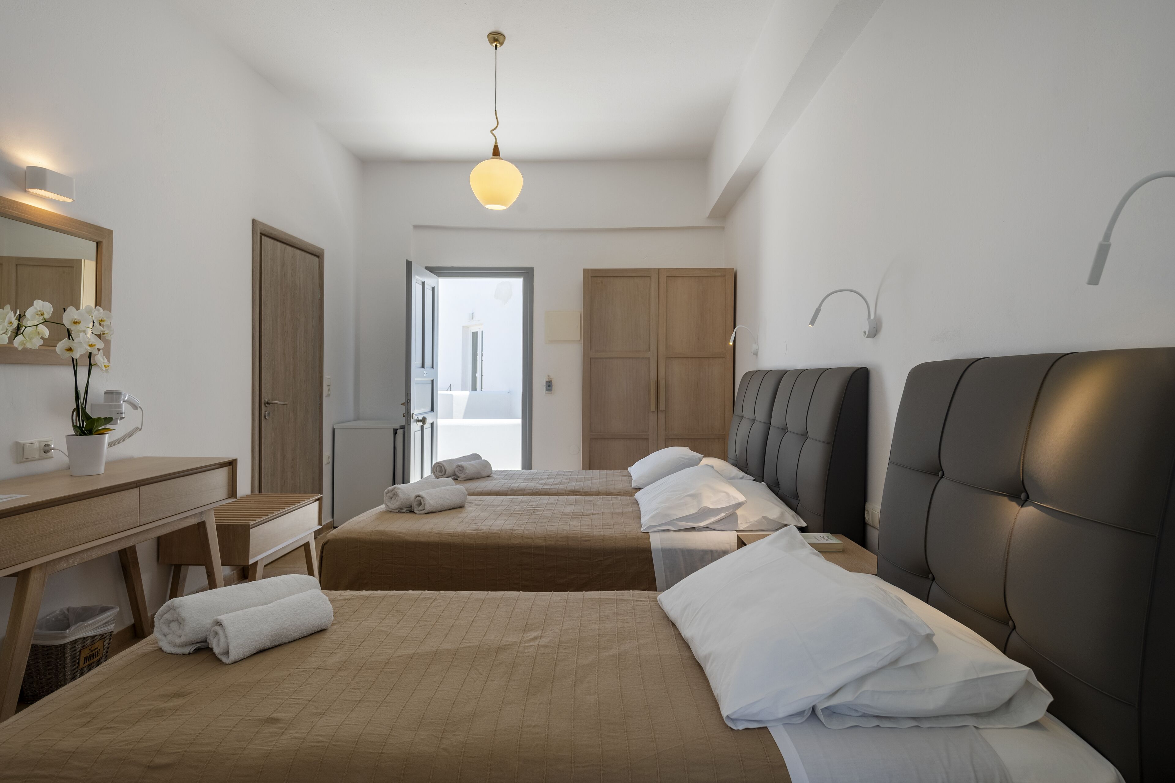A hotel room with two beds, a desk, a mirror, and a view of the outside.