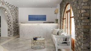 Un área de recepción con pared de piedra, un mostrador blanco, un cuadro abstracto azul y un sofá blanco con cojines.