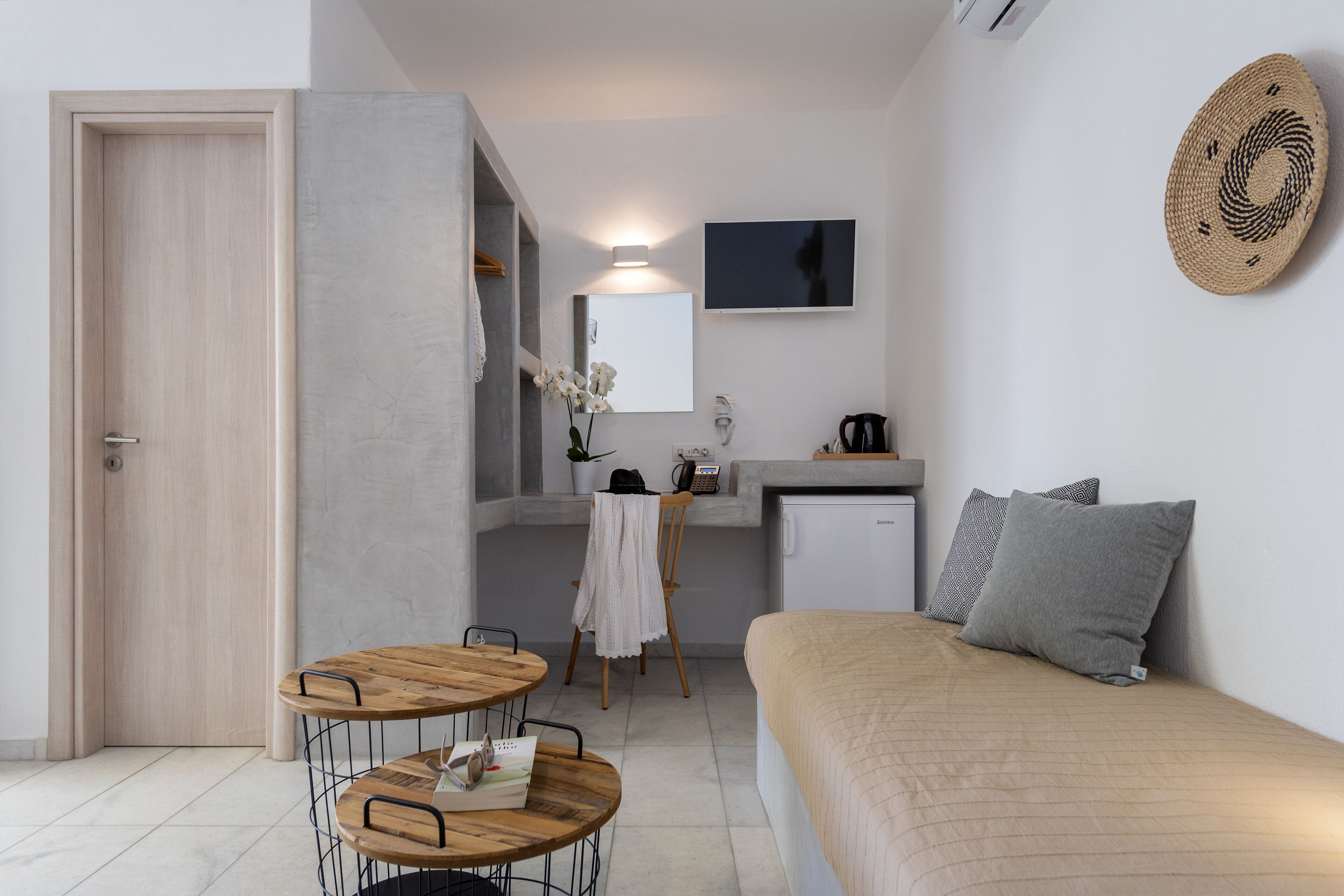 A compact room with a bed, a small table, a chair, a desk with a chair, a TV, and a wall-mounted decorative item.