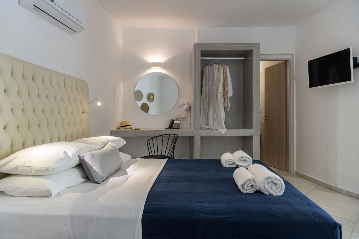 A hotel room with a bed, a desk, a mirror, and a TV.