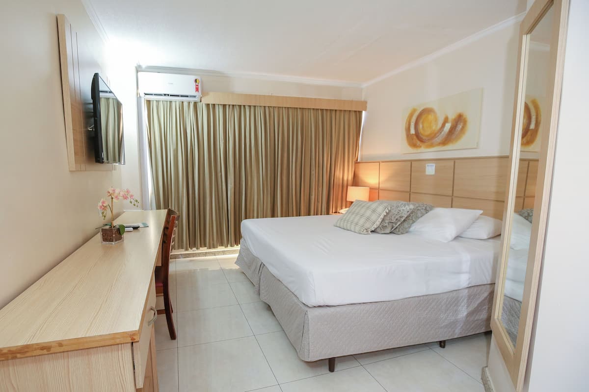 A hotel room with a bed, a desk, a TV, and a window with curtains.