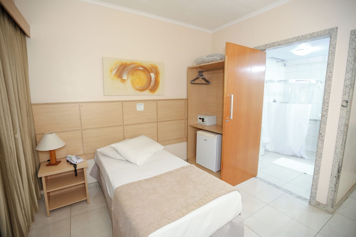 A hotel room with a bed, bedside table, lamp, and a painting on the wall.