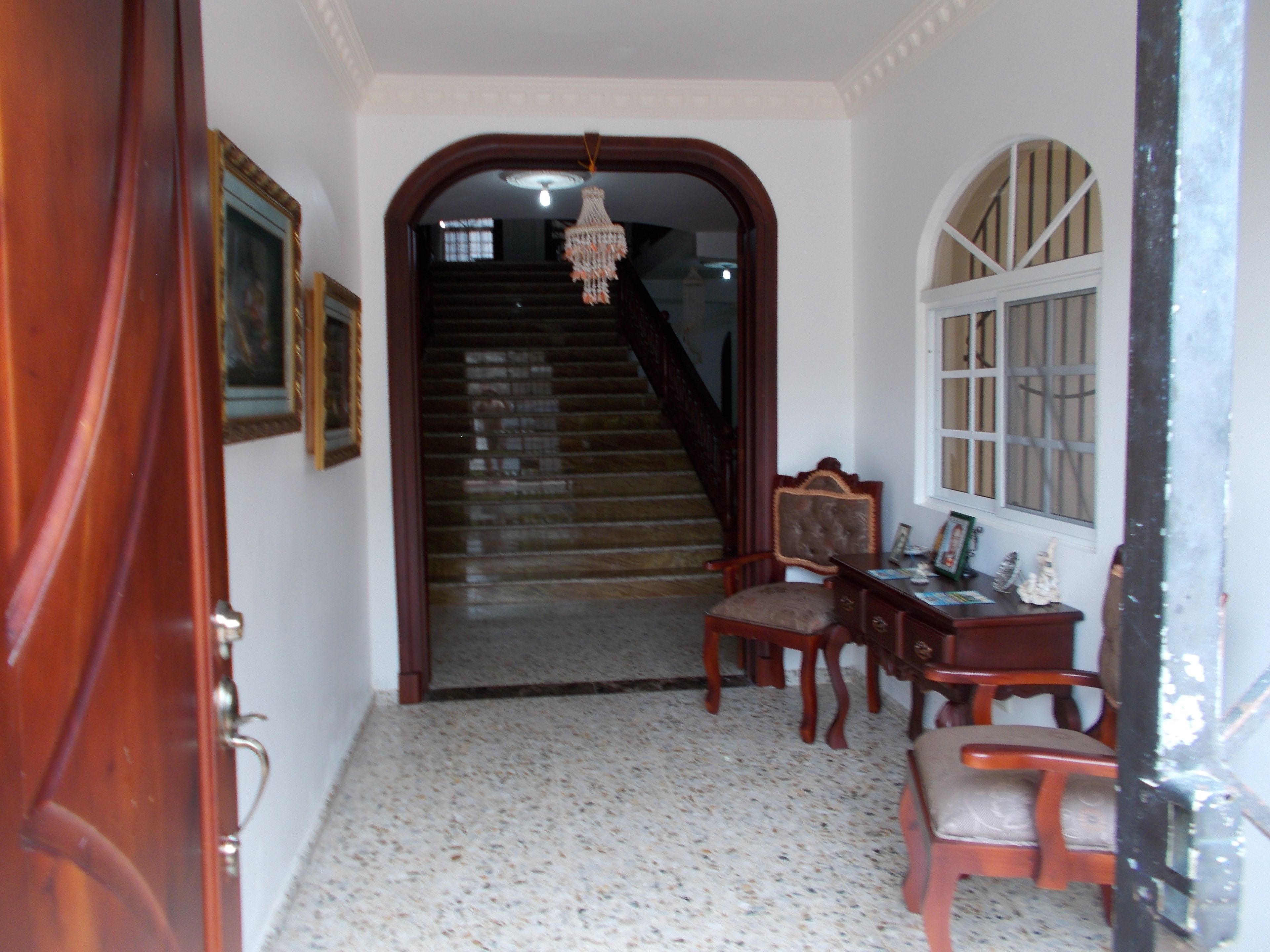 A hallway with a wooden door, a staircase, a desk with a chair, and a window.