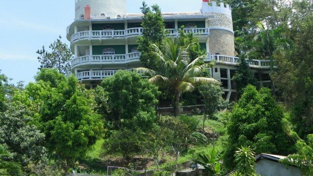 A multi-story building with balconies, surrounded by lush greenery.