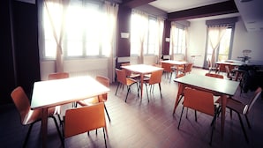 Un espace repas avec des tables et des chaises, de grandes fenêtres avec des rideaux et un radiateur.