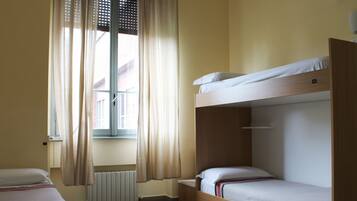 Una stanza con un letto a castello, una finestra con tende, un termosifone e un piccolo tavolo.