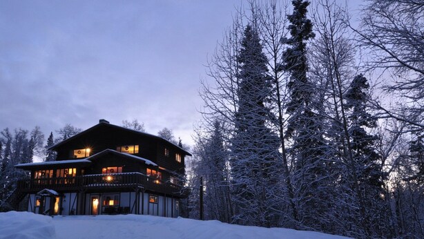 A large, multi-story lodge with a balcony, surrounded by snow-covered trees. - Talkeetna Chalet (Talkeetna)