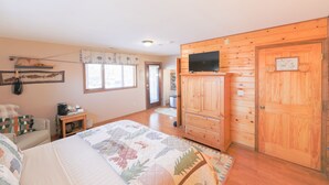 A bedroom with a bed, a wooden wardrobe, a television on a stand, a window, and a door. - Talkeetna Chalet (Talkeetna)