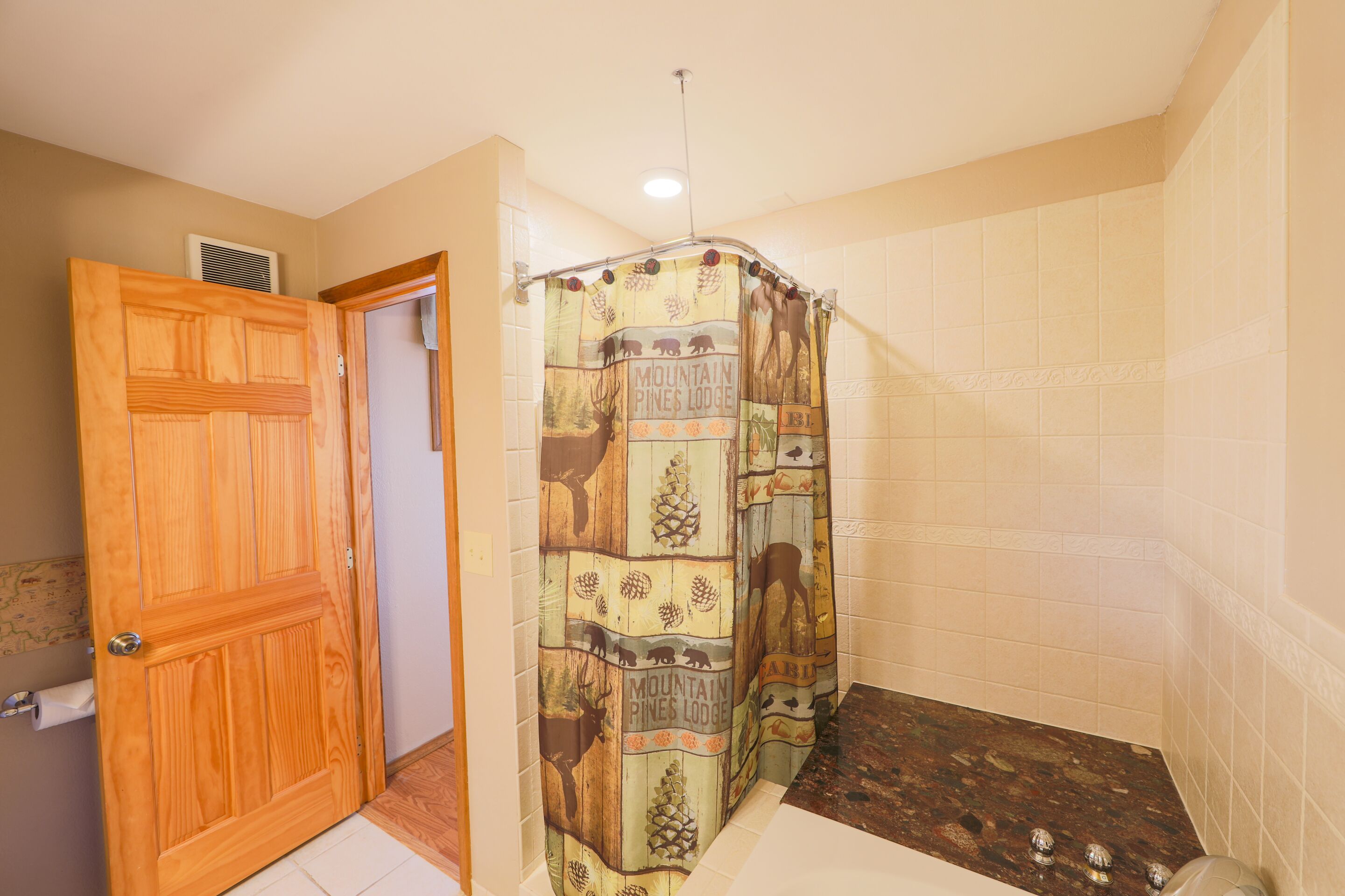 Un baño con cortina de ducha, puerta de madera y pared de azulejos.