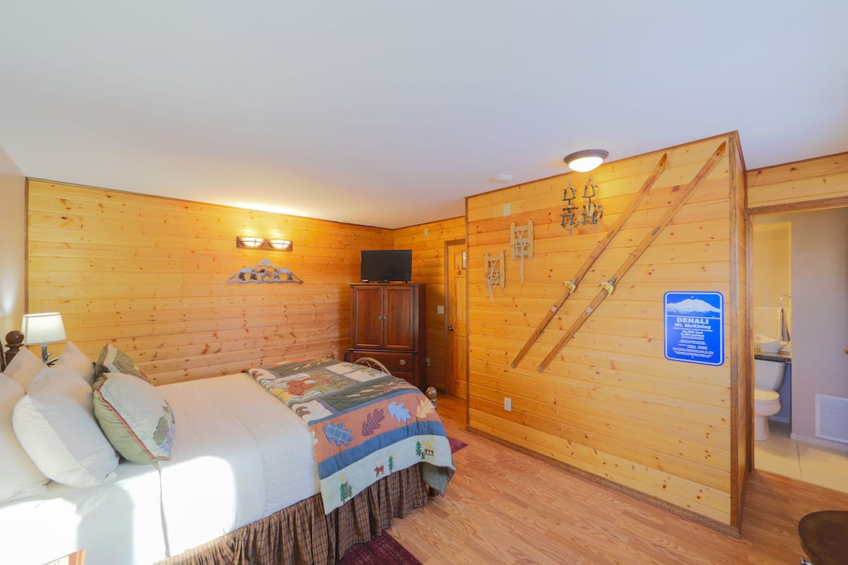 A wooden-paneled room with a bed, a cabinet, and a sign indicating a Denali ski area.