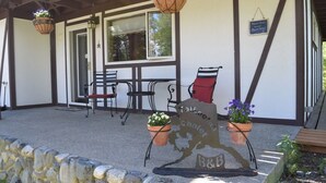 A covered outdoor seating area with stone walls, a table with chairs, hanging flower baskets, and a welcome sign. - Talkeetna Chalet (Talkeetna)