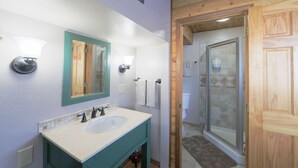 A bathroom with a sink, mirror, and wooden door leading to a shower area. - Talkeetna Chalet (Talkeetna)